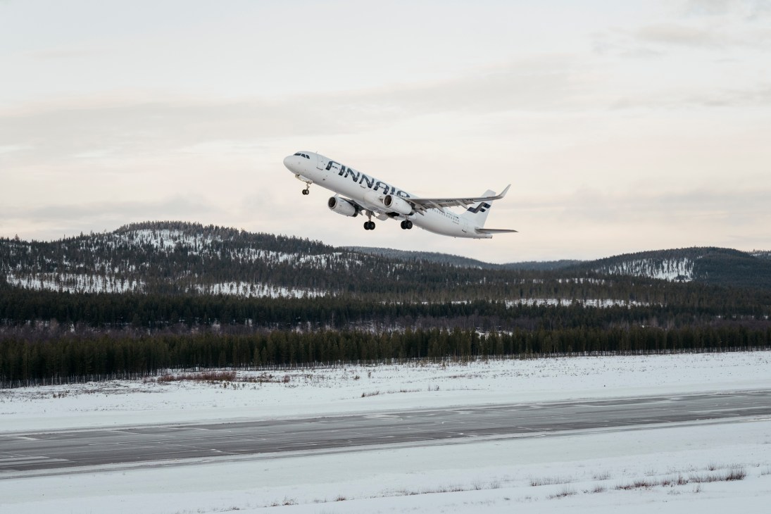 Finnair aircraft taking off from snow-covered runway with forested hills in background at Ivalo Airport
