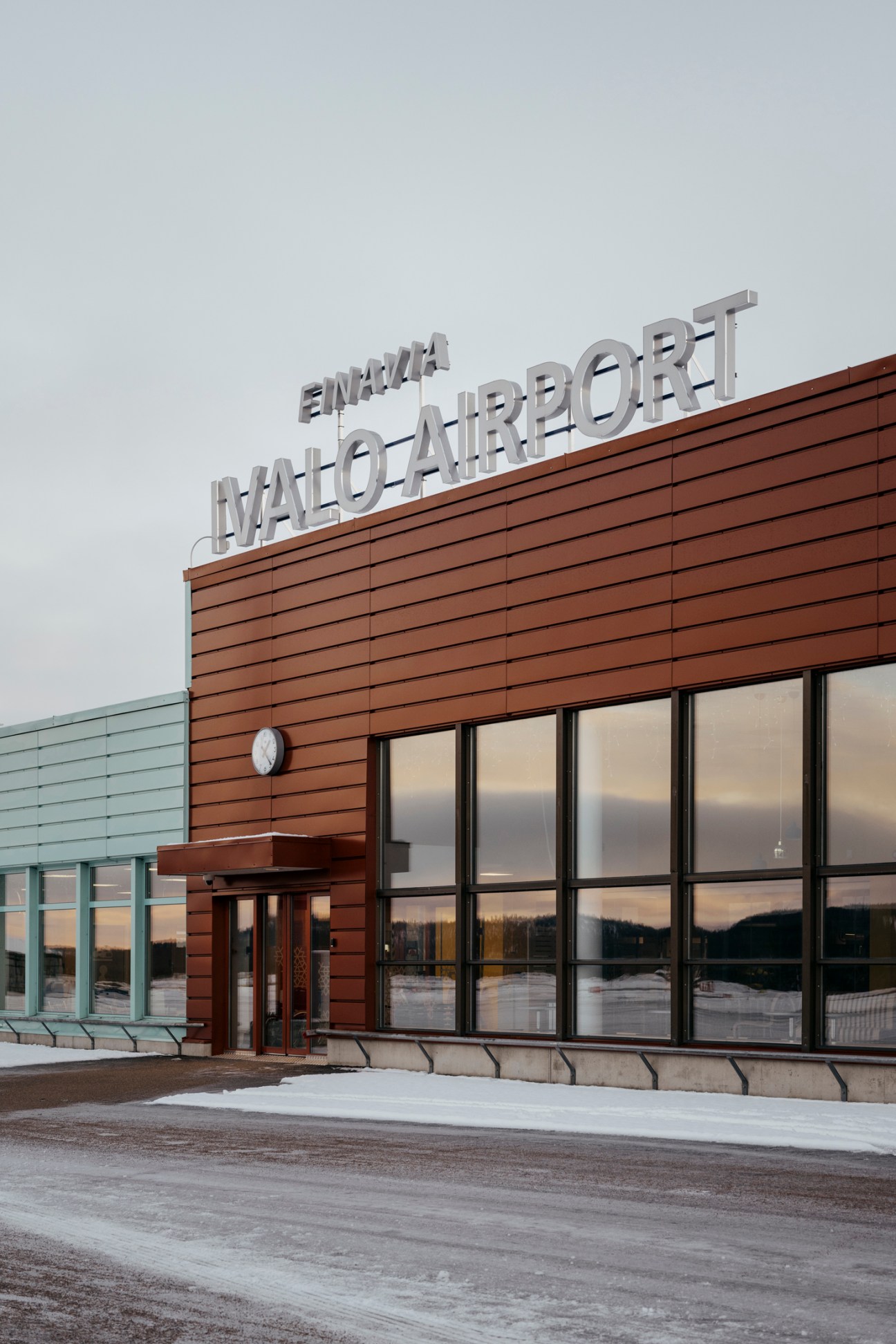 Modern airport terminal building with wood-paneled facade and large glass windows showing Ivalo Airport signage