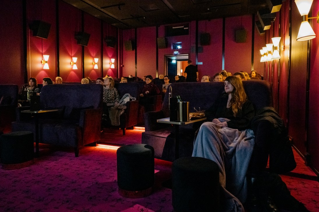 People watching a film in a darkly lit cinema with plush seating, red walls, and ambient lighting