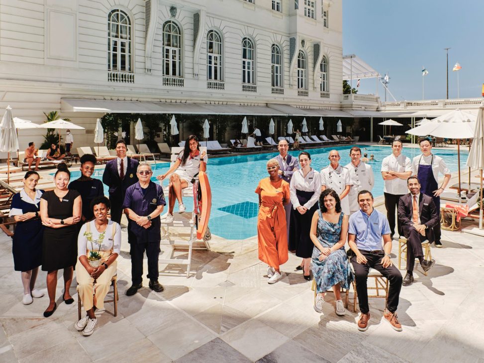 Group photo of Copacabana Palace hotel staff members standing together by pool in white neoclassical building