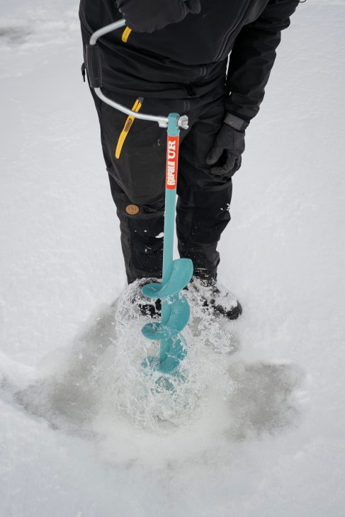 Person using ice auger to drill hole through frozen lake surface