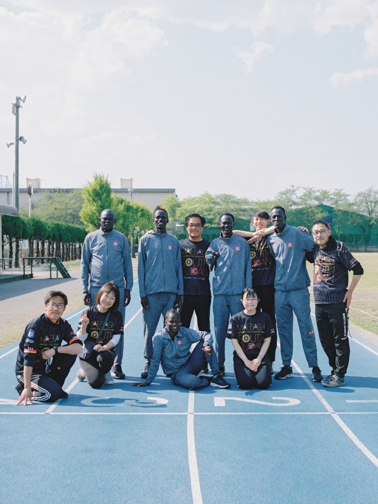 Group photo of South Sudanese Olympic athletes and Japanese supporters on a running track in Maebashi
