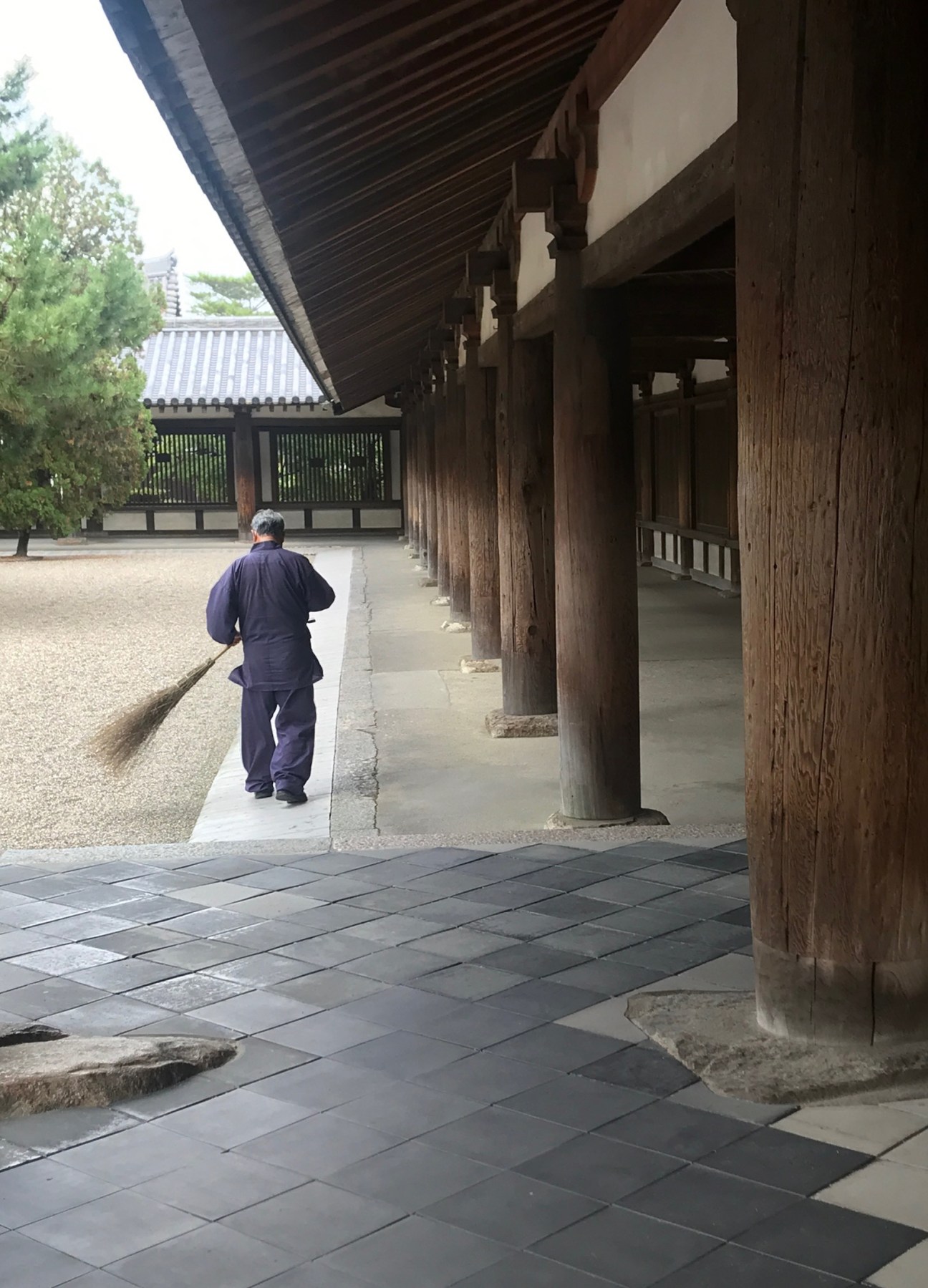 Person in traditional Japanese clothing sweeping wooden temple corridor with stone courtyard at Horyu-ji temple