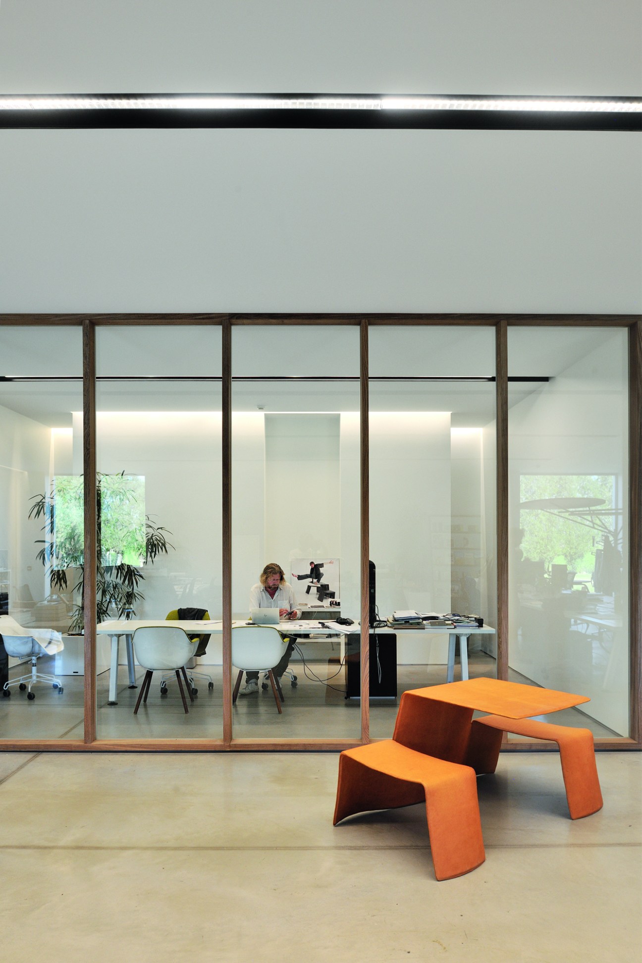 Modern office space with glass walls, white furniture, and orange geometric seating in foreground