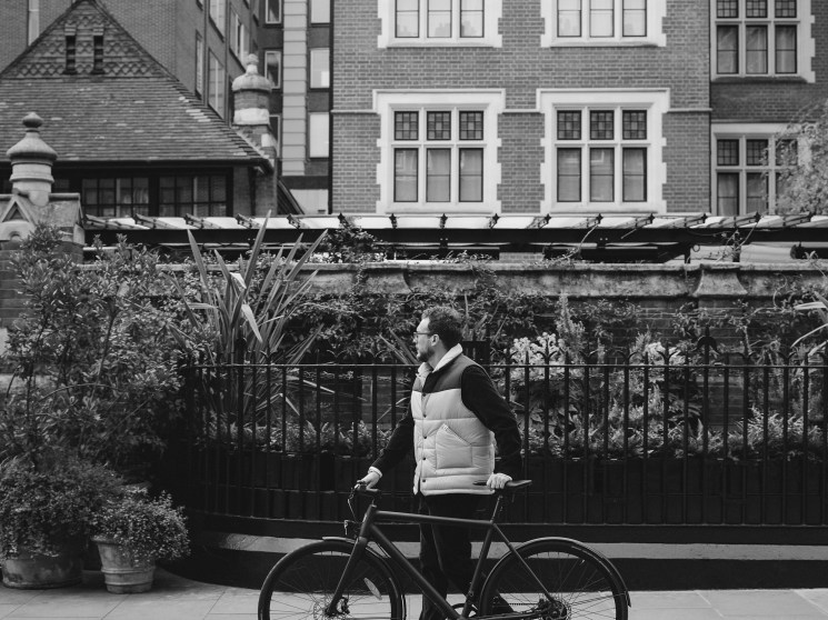Black and white photo of a person with a bicycle on a city street.