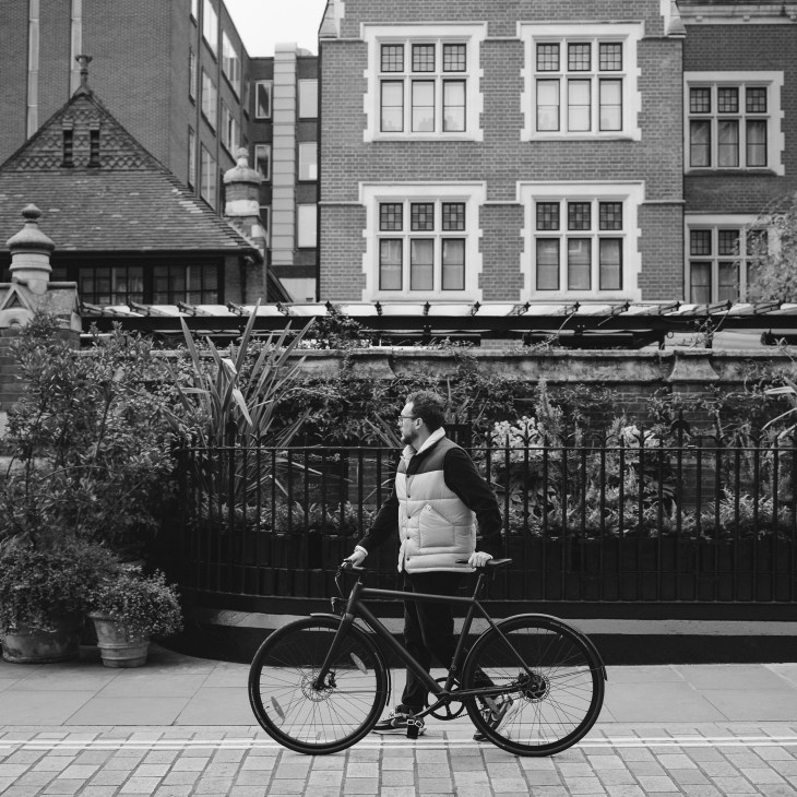 Man with bicycle standing on sidewalk in front of urban buildings