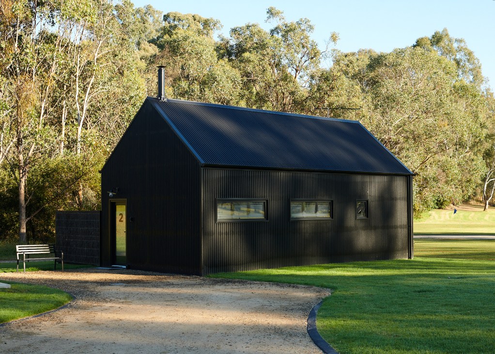 Modern black corrugated metal accommodation building with gabled roof and windows set in grassy landscape