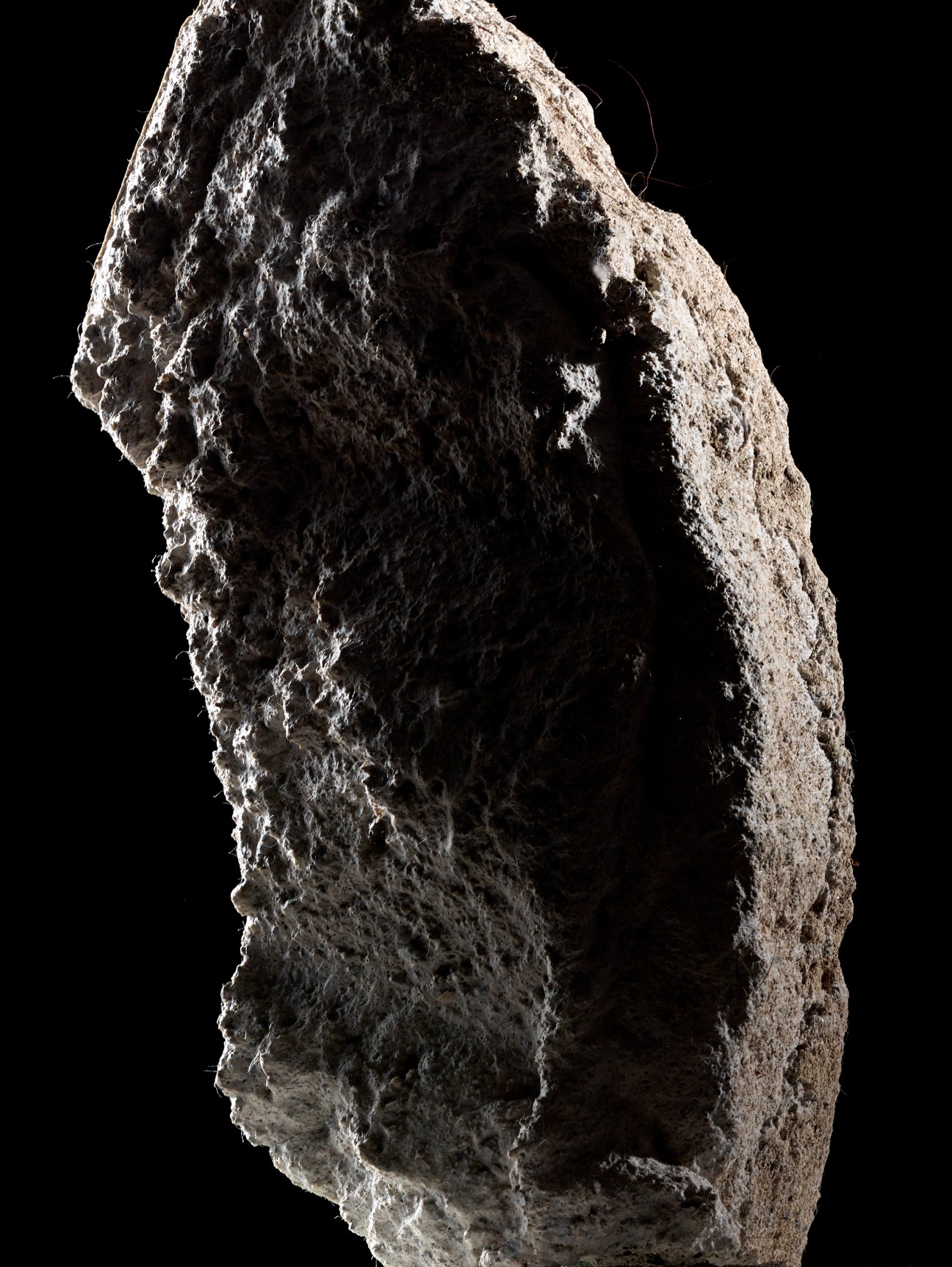 Rough-textured gray concrete or cement material sample with irregular, porous surface against black background