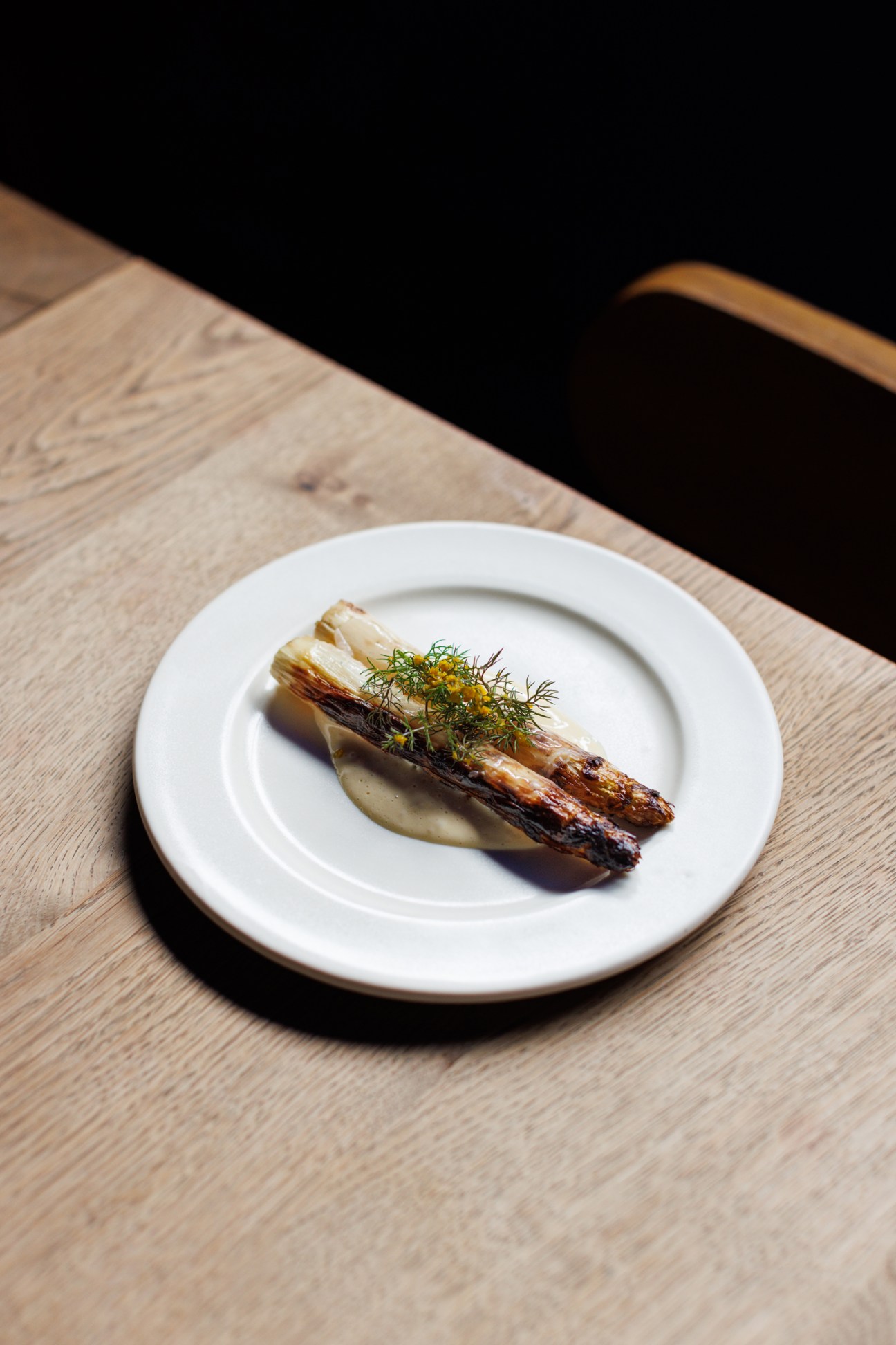 Grilled asparagus spears with herb sauce and dill garnish on white plate on wooden table