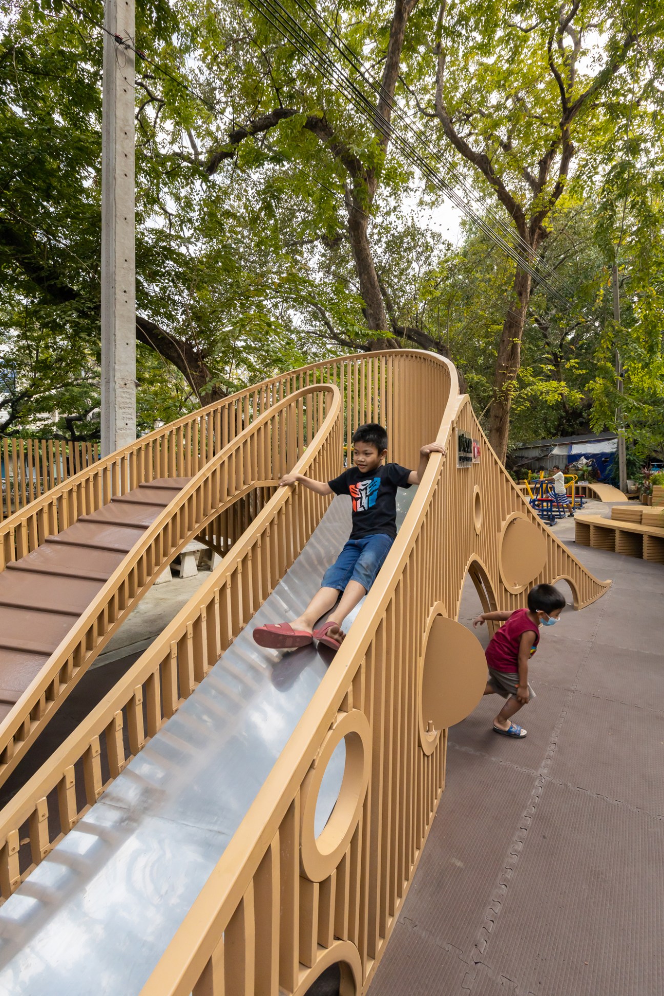 Children playing on Choduk Playground's wooden sculptural slide and climbing structures in Bangkok