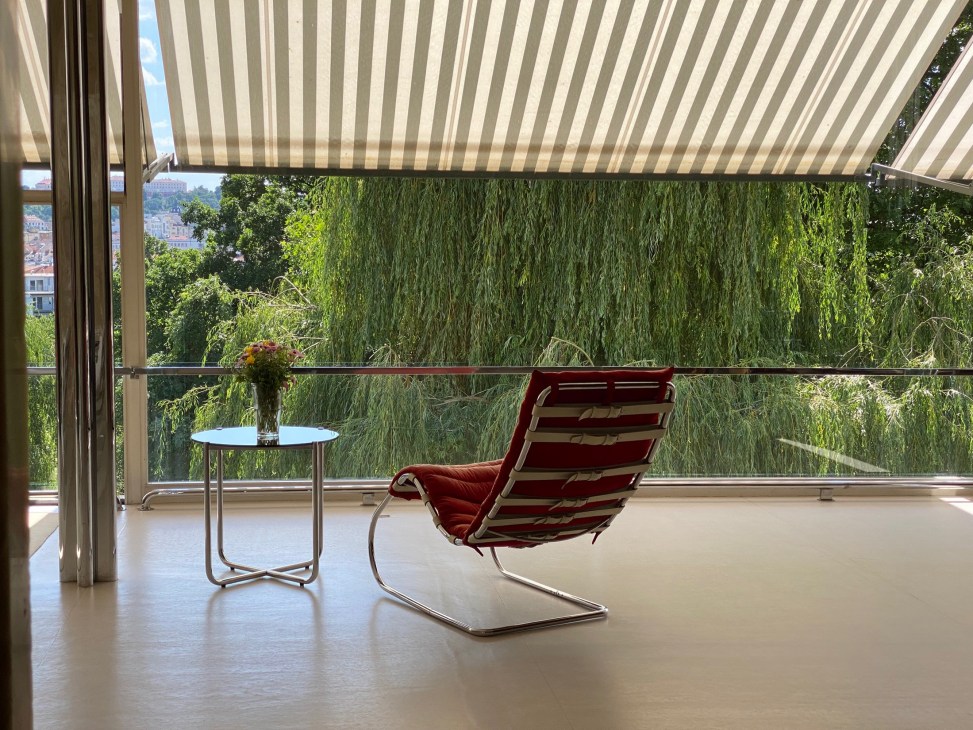 Modern interior with red cantilever chair, small round table, and floor-to-ceiling windows overlooking green landscape
