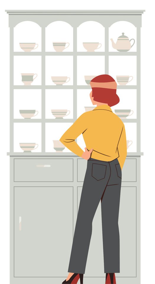 Person in yellow sweater and dark pants standing in front of china cabinet displaying teacups and dishes