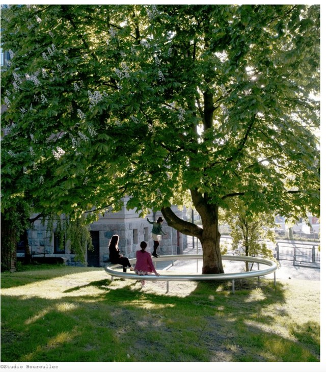 Circular white bench surrounding a large tree in a park with two people sitting on it