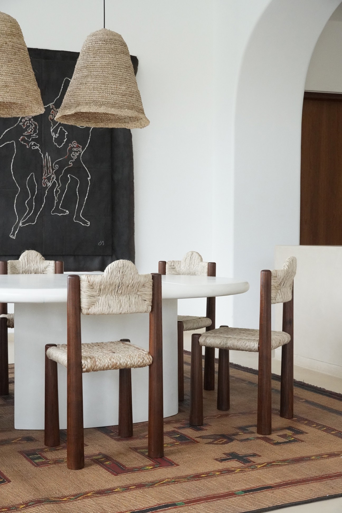 Dining room with woven jute chairs, pendant lights, patterned rug and artwork on white walls
