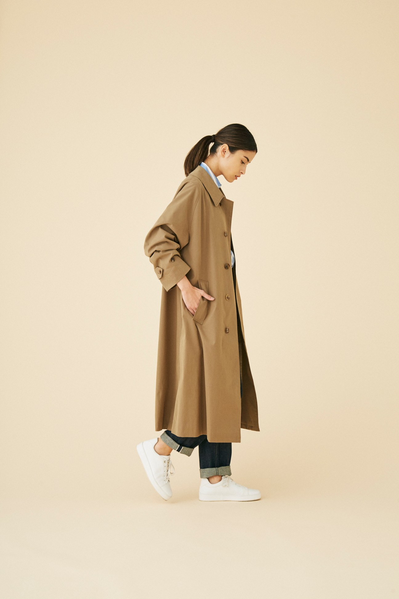 Woman wearing beige trench coat by Leno against neutral background