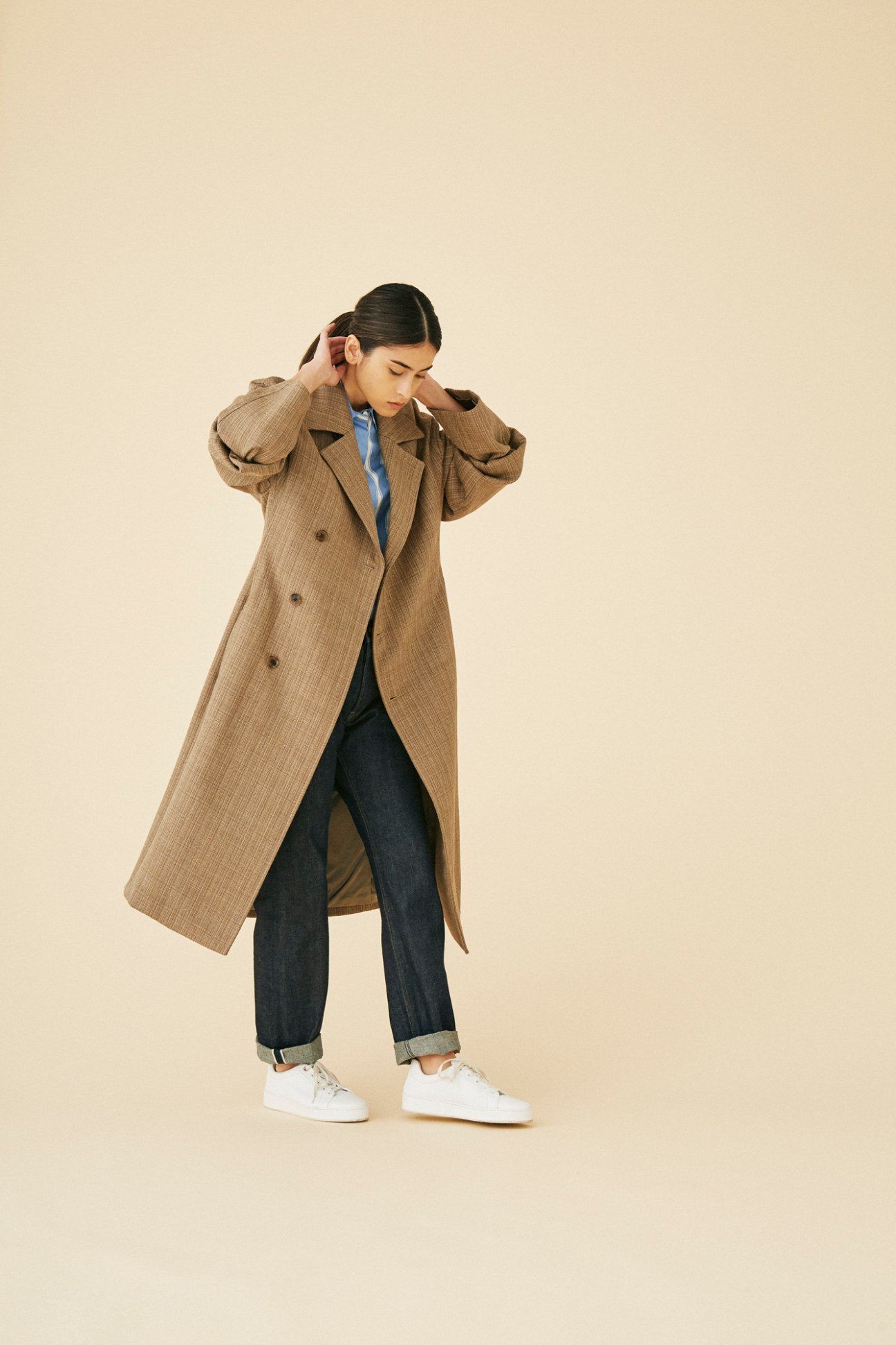 Man wearing elegant brown double-breasted trench coat by Auralee against clean background