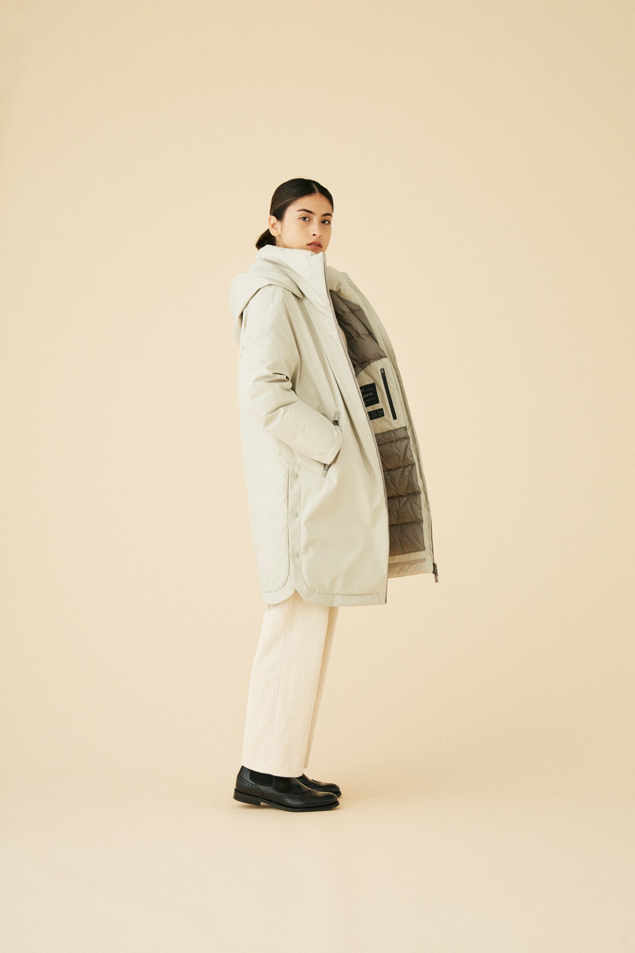 Woman wearing beige reversible coat by Herno showing quilted interior lining in studio portrait