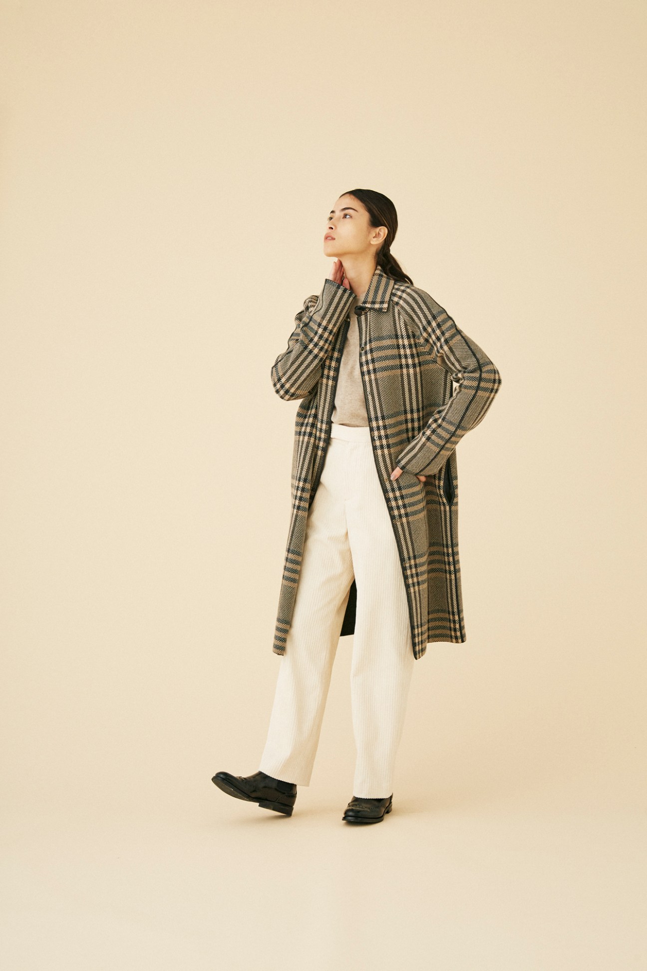 Woman wearing long plaid coat by Loro Piana over cream outfit against beige background