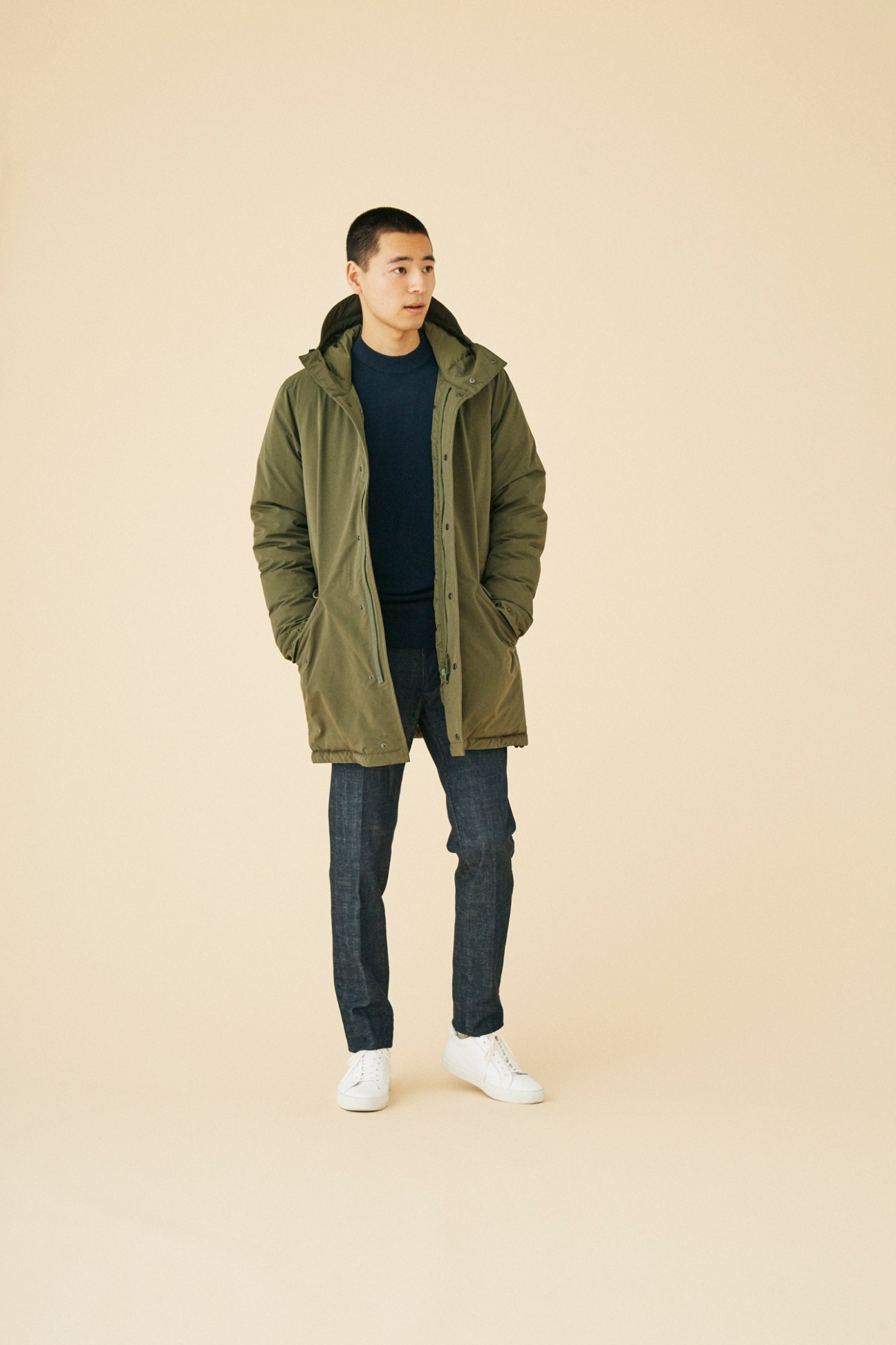 Man wearing streamlined olive green parka by Aspesi with hood over dark sweater and jeans