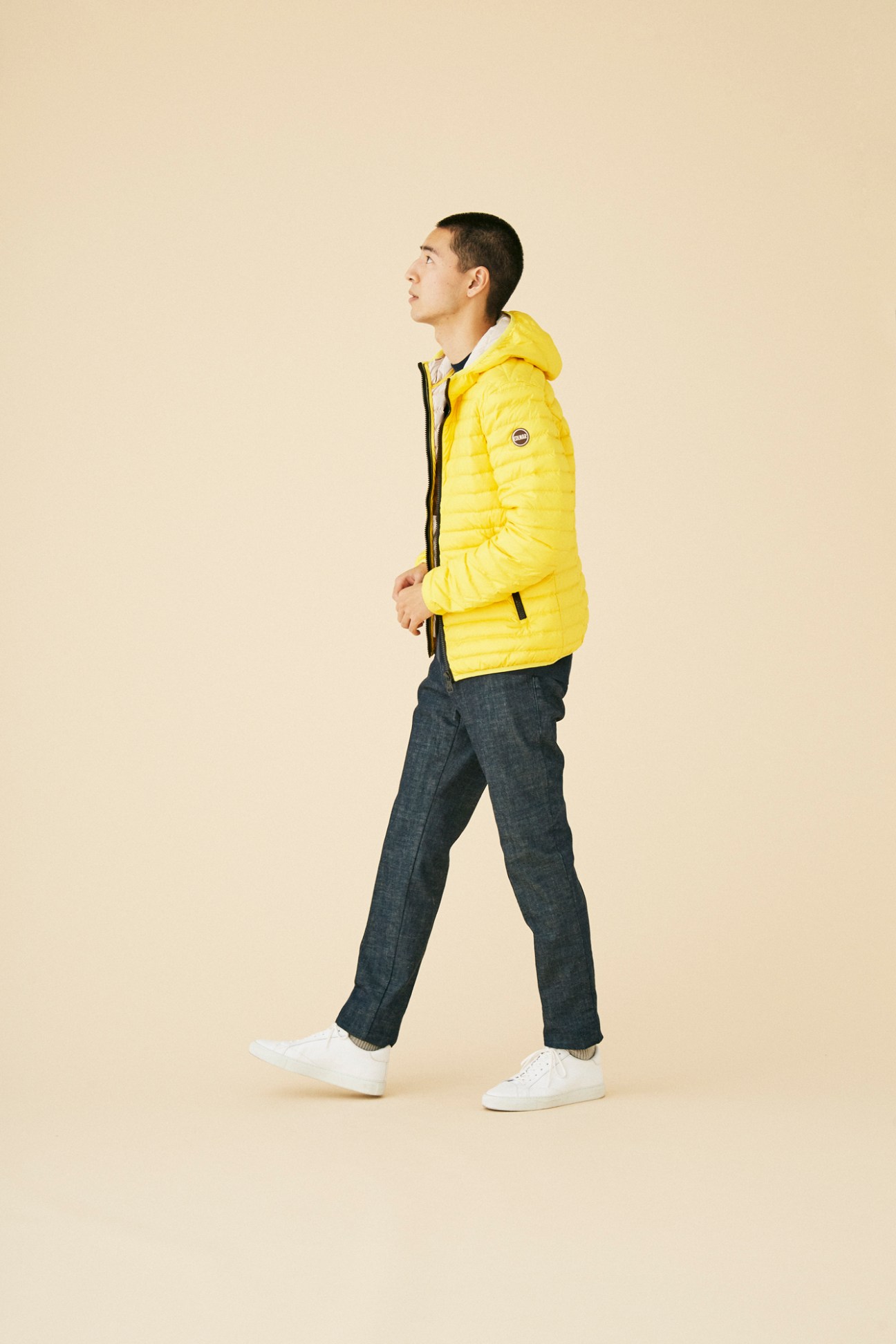 Man wearing bright yellow quilted puffer jacket by Colmar walking against beige background