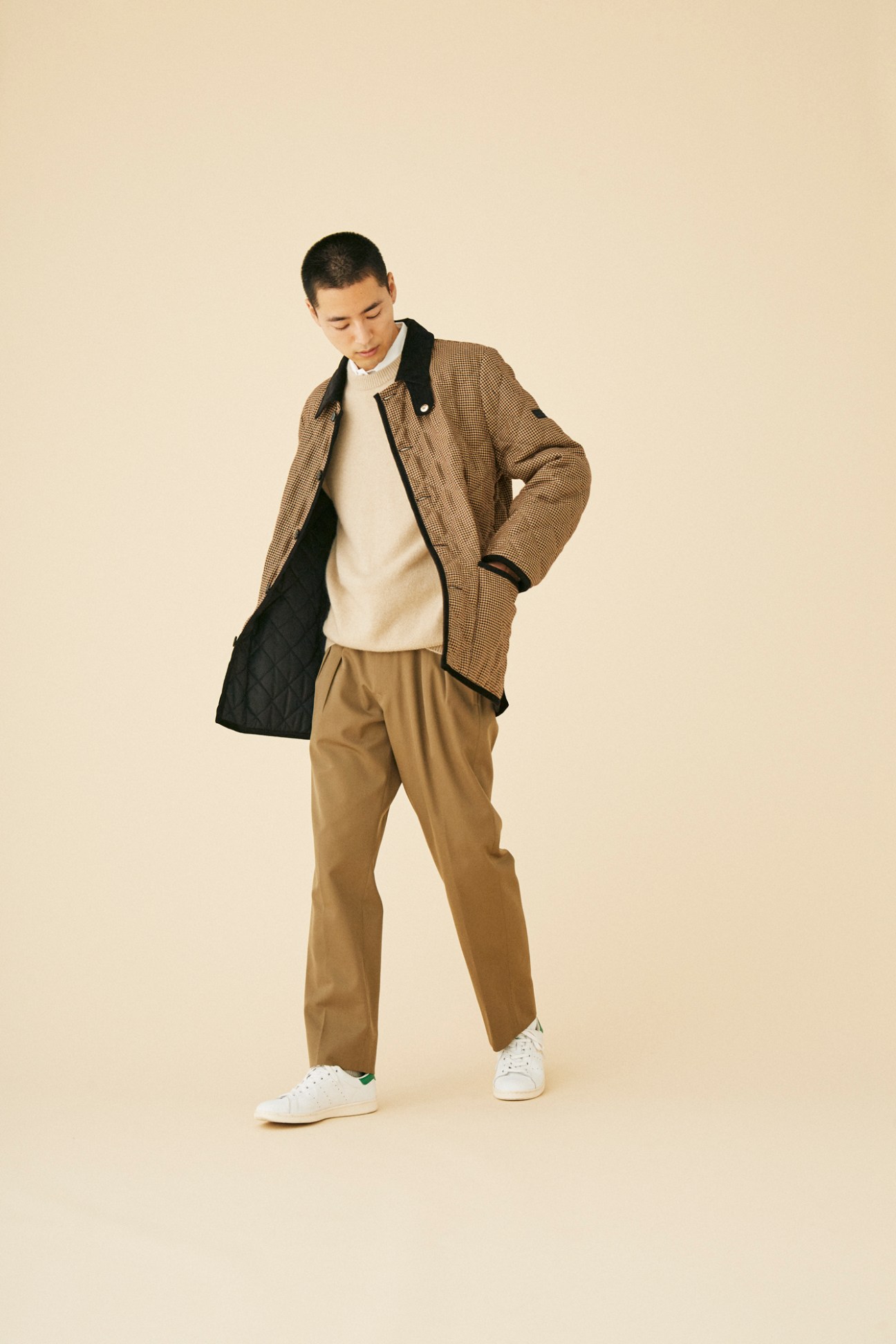 Man wearing brown houndstooth Mackintosh jacket over cream sweater with tan trousers and white sneakers