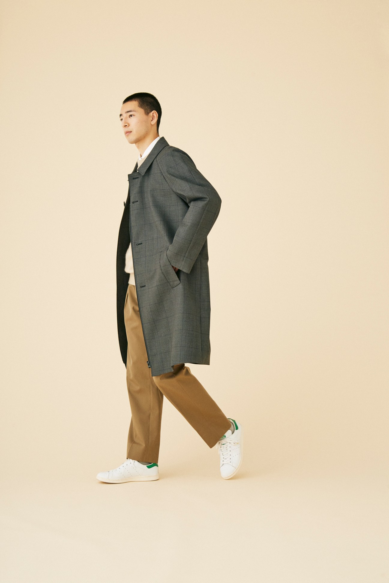 Man wearing structured grey coat by Emporio Armani with camel trousers and white sneakers in studio lighting