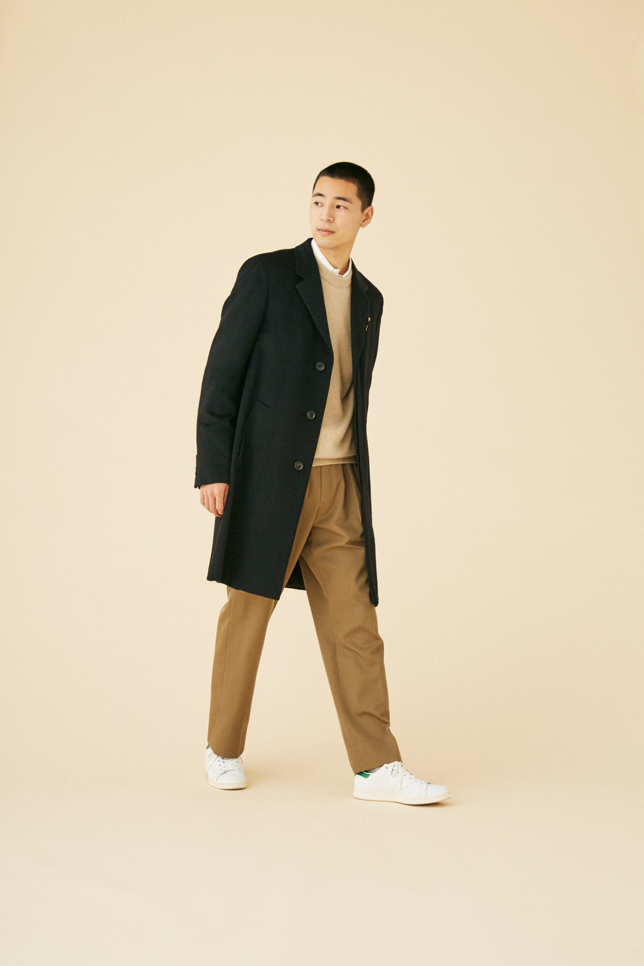 Man wearing long black double-breasted coat by Louis Vuitton with beige sweater and brown trousers