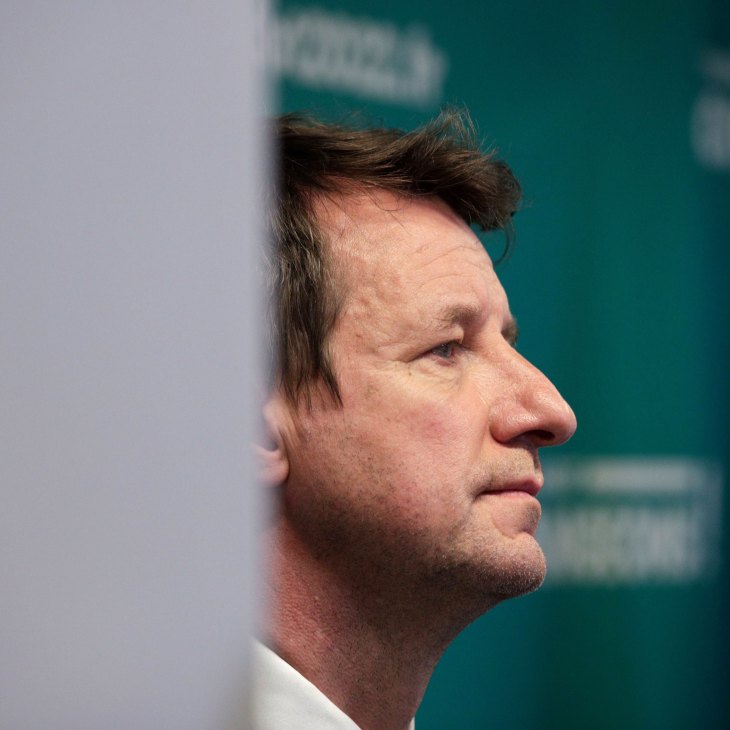 Profile view of a man in a white shirt speaking at what appears to be a political event or press conference