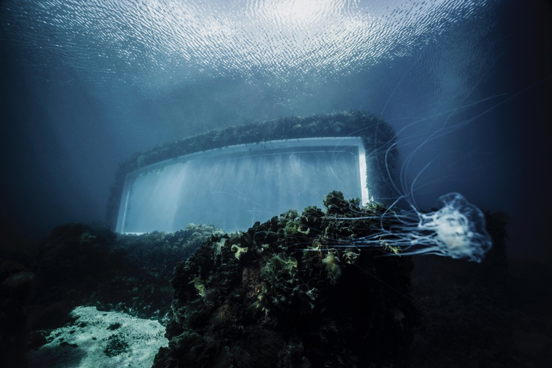 Underwater dining room with large windows showing ocean life and coral formations on seafloor
