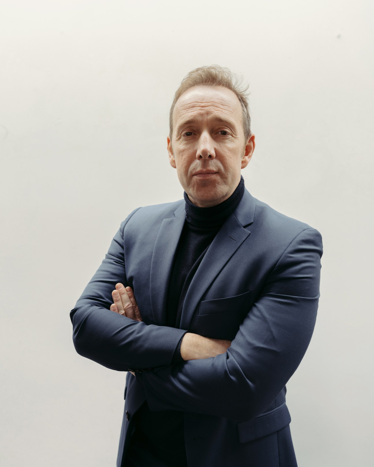 Stéphane Albouy in a navy blue suit with crossed arms standing against a white background