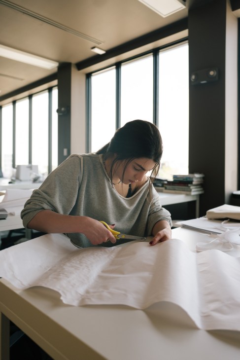Student cutting fabric at a design table in a bright studio classroom at Istituto Marangoni.