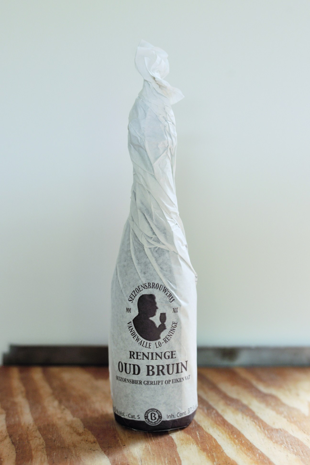 White paper-wrapped beer bottle with Seizoensbrouwerij logo and Oud Bruin label on wooden surface