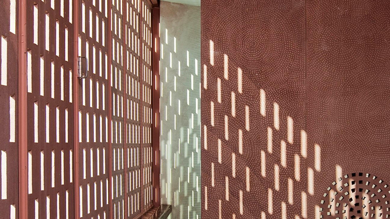 Sunlight filtering through perforated red sandstone screens creating geometric shadow patterns on walls