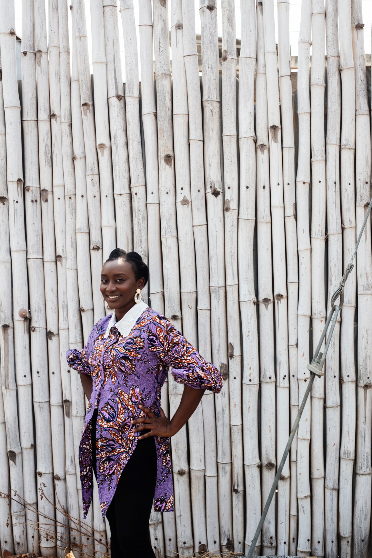 Ruth-Anne Richardson, architect, poses in a colorful purple patterned dress against white bamboo backdrop