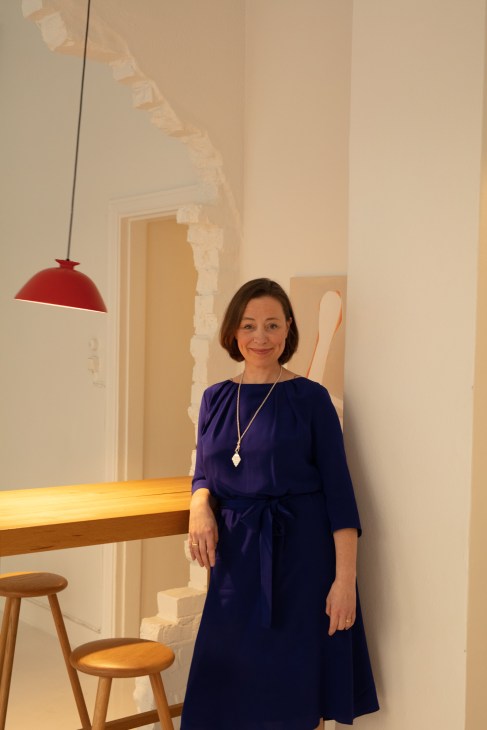 Woman in navy dress standing at wooden counter beneath red pendant lamp in minimalist interior
