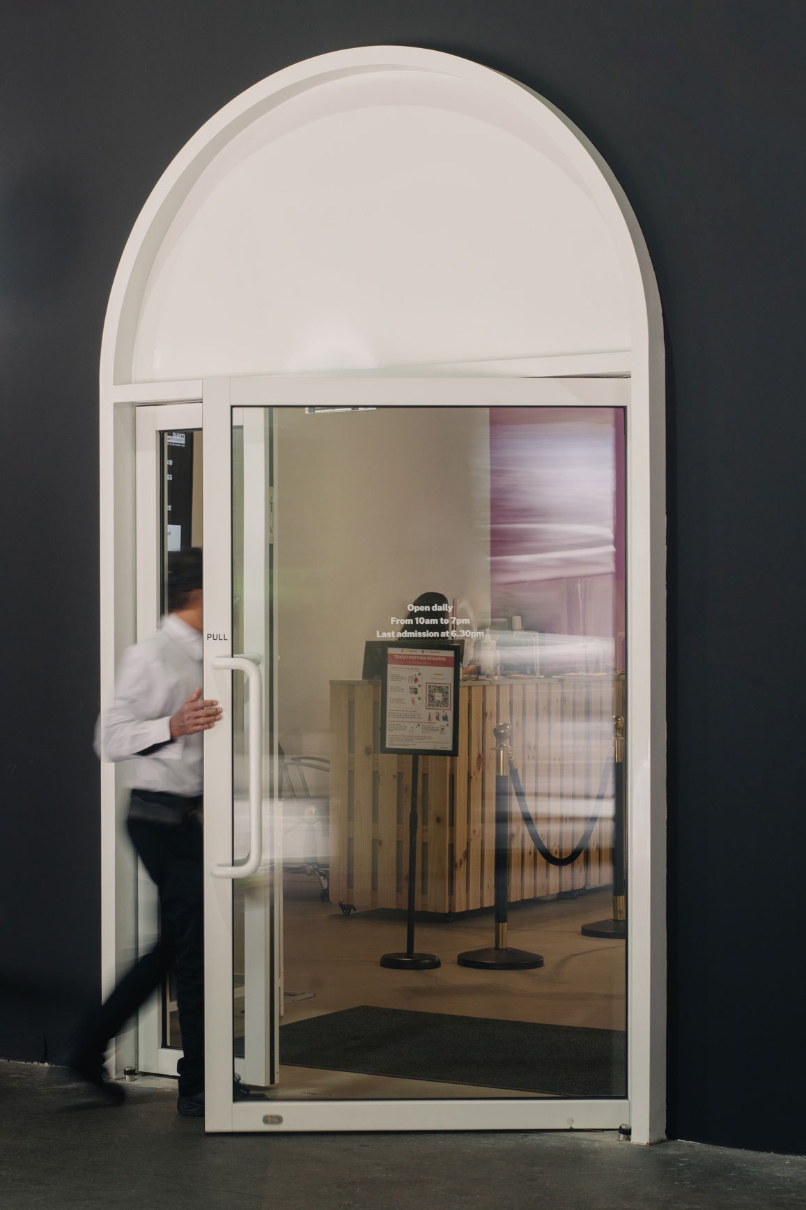 Person entering a gallery lift installation with arched doorway and wooden sculptural element inside.
