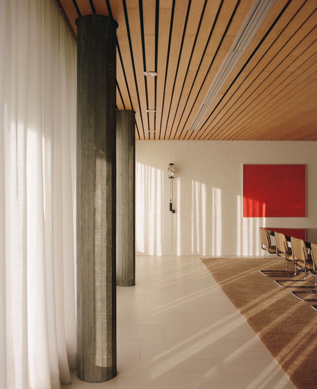 Interior meeting room with wooden slatted ceiling, concrete columns, and red abstract painting on white wall