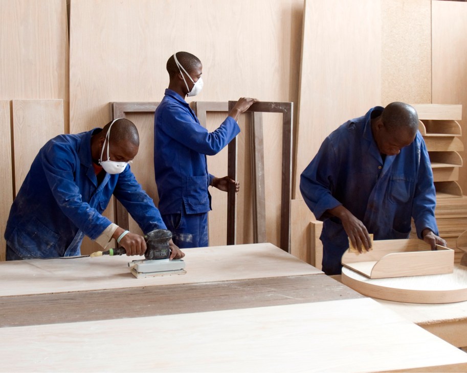 Craftspeople working with wood in a workshop, sanding and shaping furniture components.