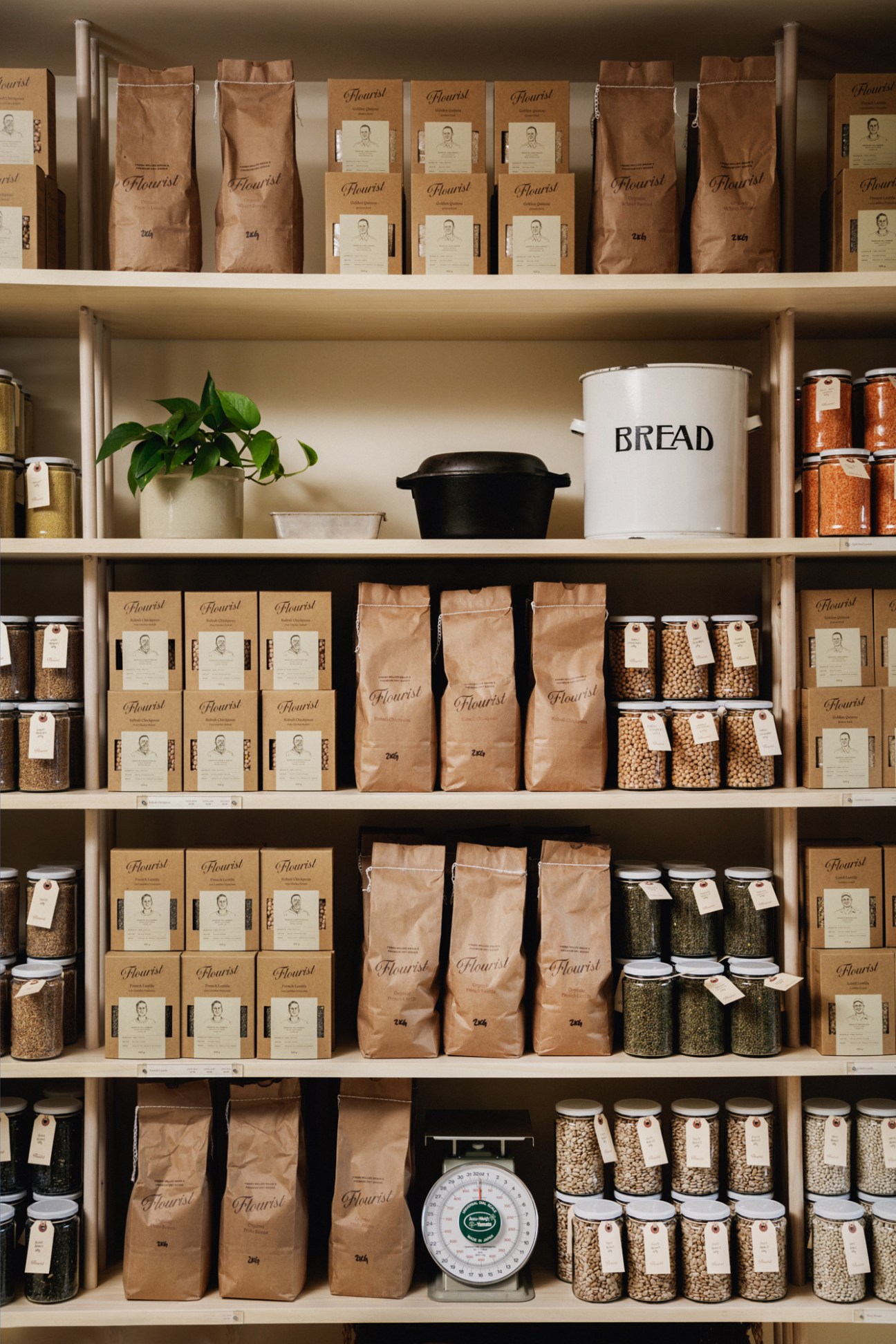 Organized shelves displaying brown paper bags and glass jars of flour, grains and baking ingredients at Flourist bakery