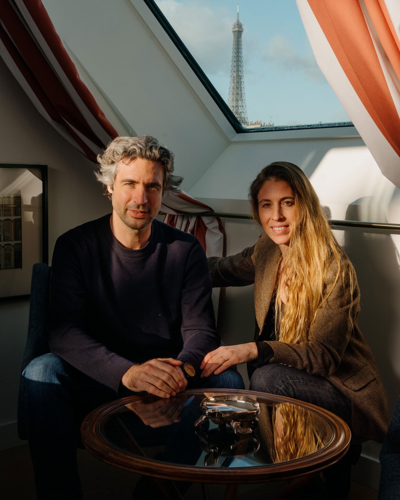Louis and Anouk Solanet, founders of Orso hotel, sitting together in a Parisian room with a view of the Eiffel Tower through the skylight