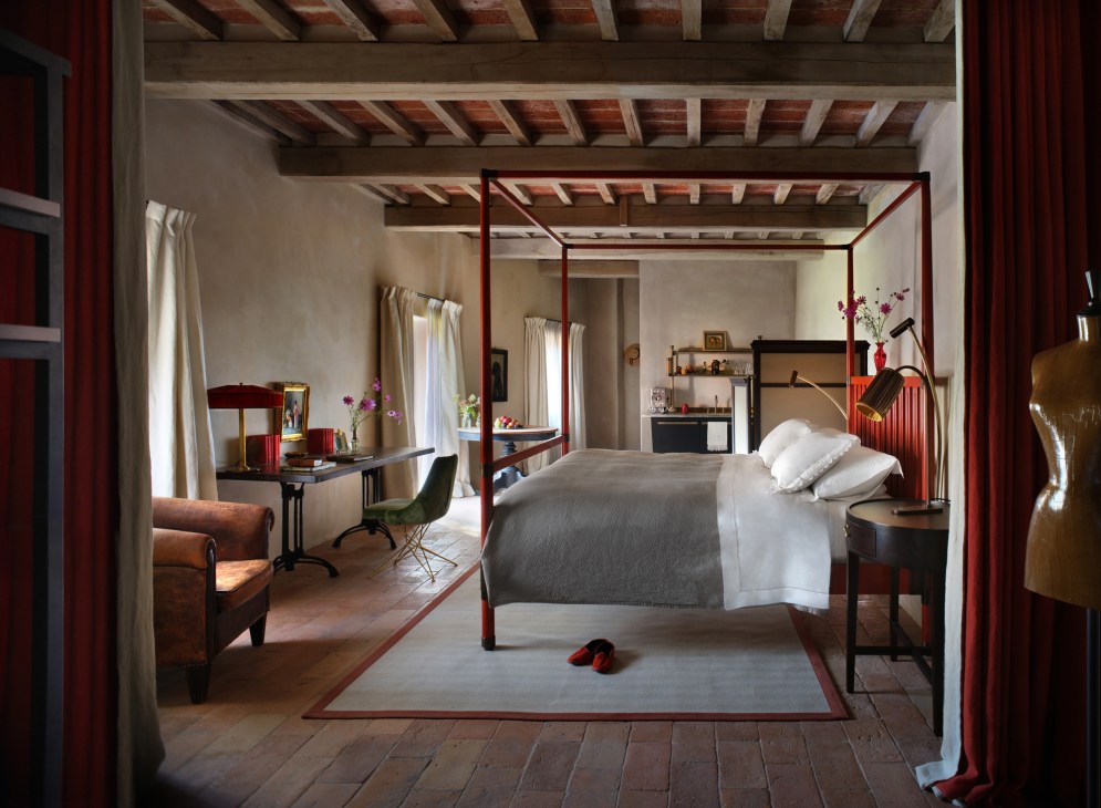 Hotel bedroom with red four-poster bed, exposed beam ceiling, and custom Italian furnishings
