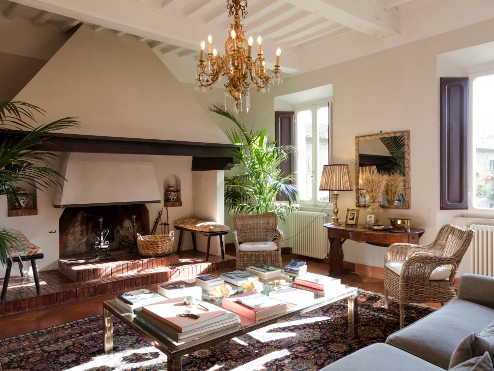 Elegant living room interior with ornate chandelier, wicker furniture, fireplace, and antique furnishings