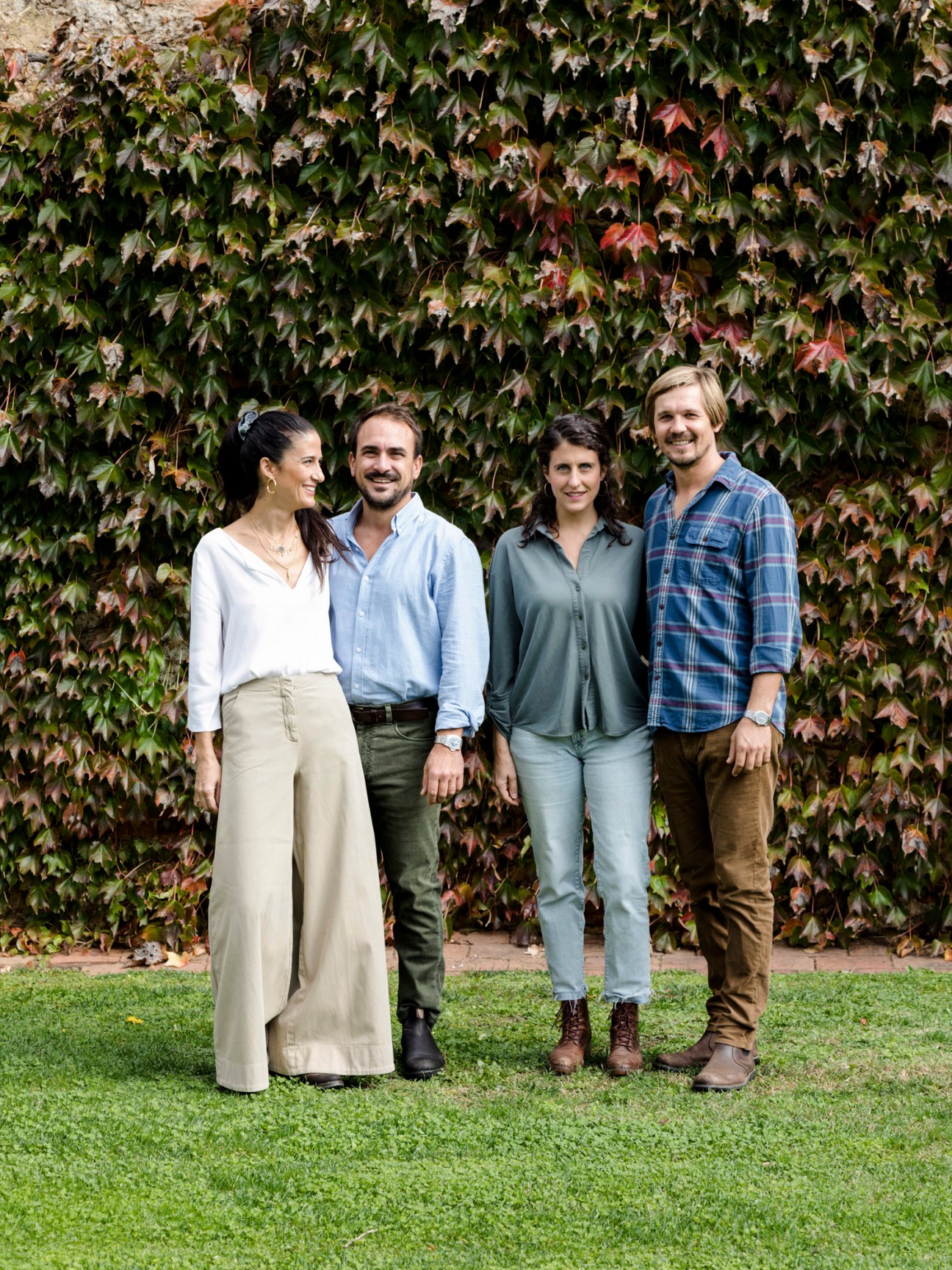Four people standing together on grass in front of ivy-covered wall at countryside resort