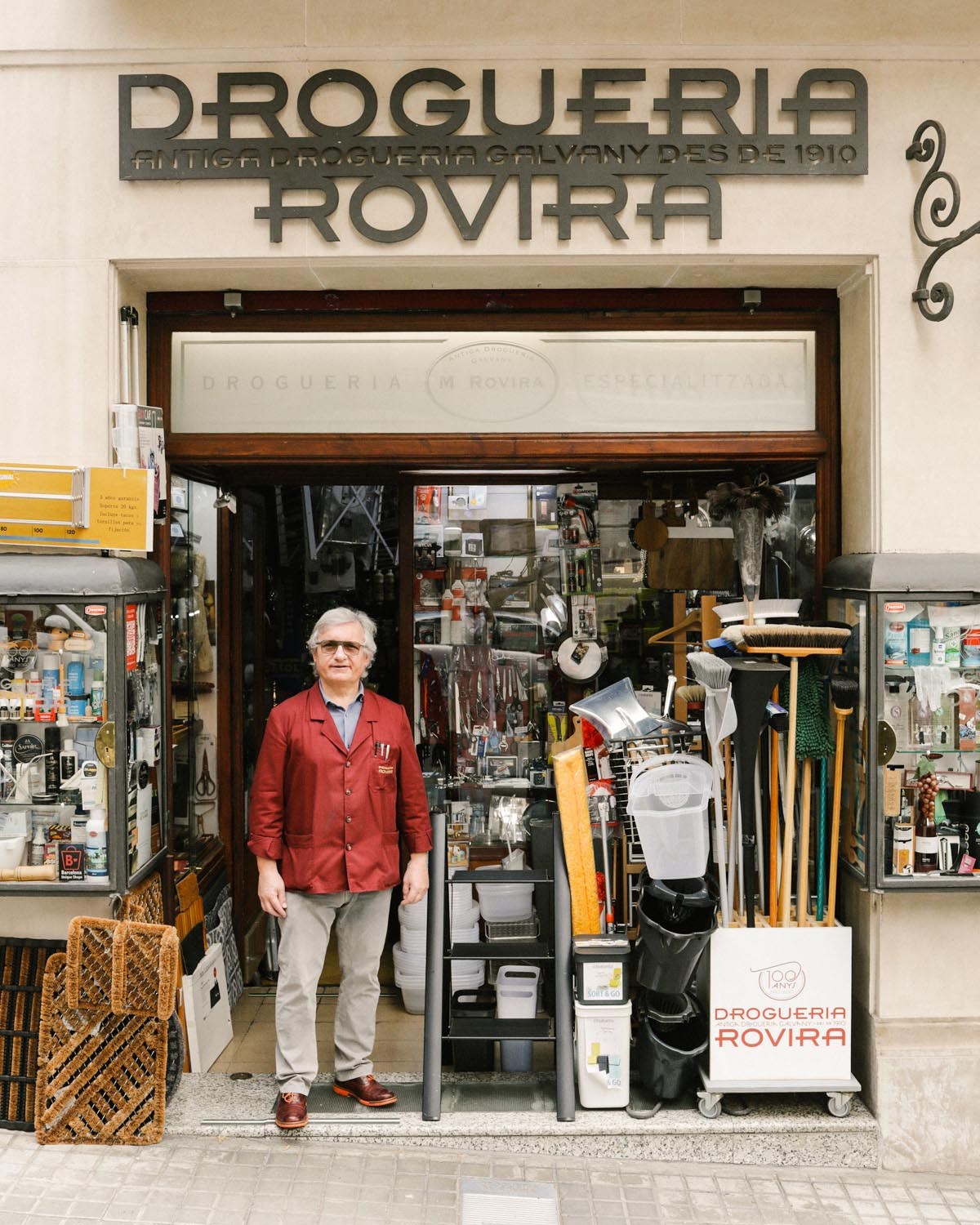 Man in red cardigan standing in doorway of hardware store filled with organized shelves of household items