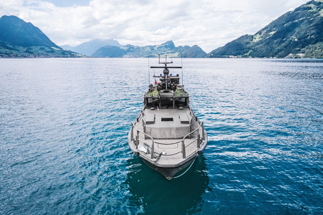 Gray military patrol boat on blue water surrounded by mountains