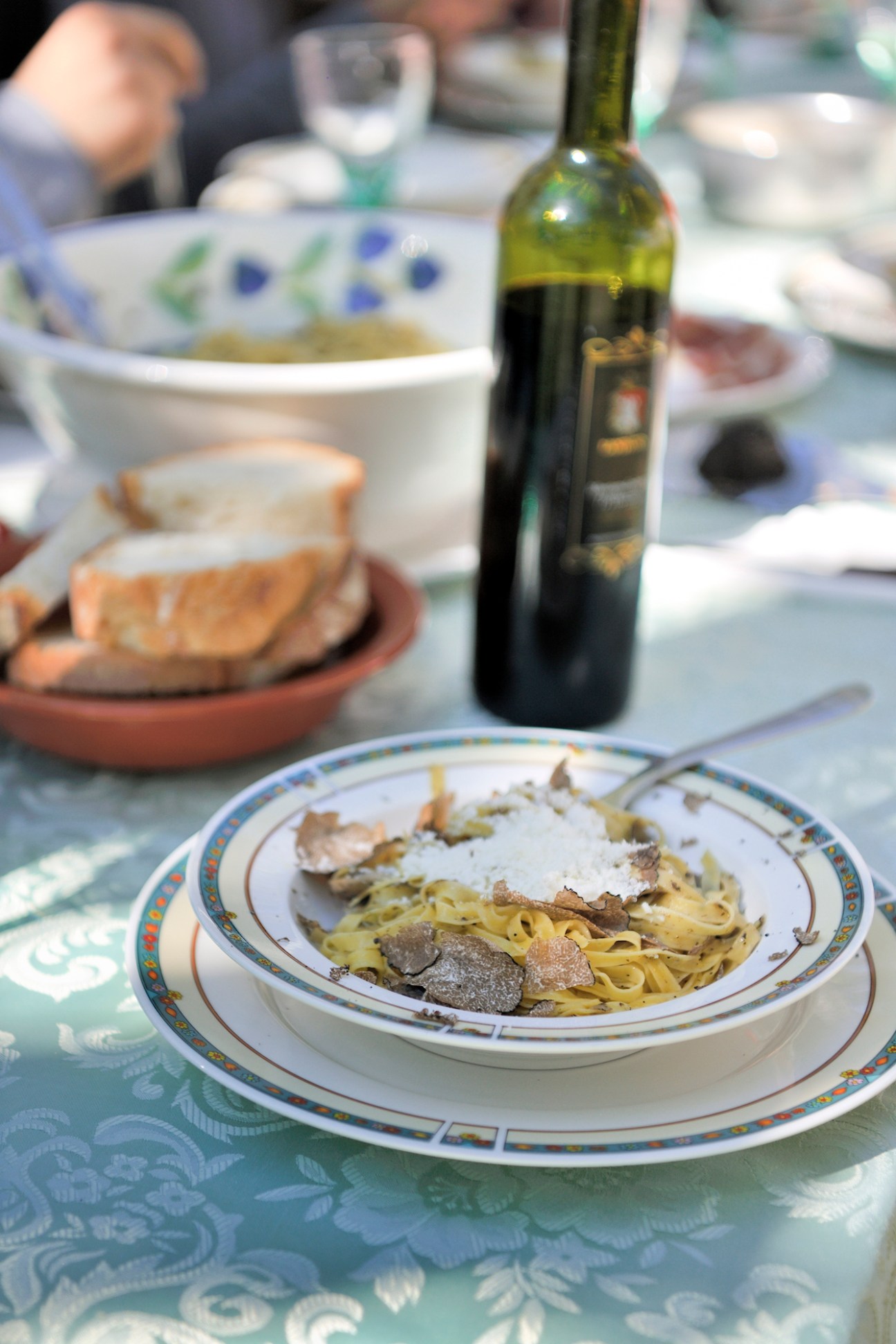 Pasta with truffle shavings and cheese on a decorative plate with wine bottle at a table setting.