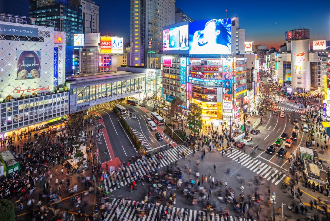 Aerial view of busy Shibuya crossing at night with crowds of pedestrians and illuminated digital billboards