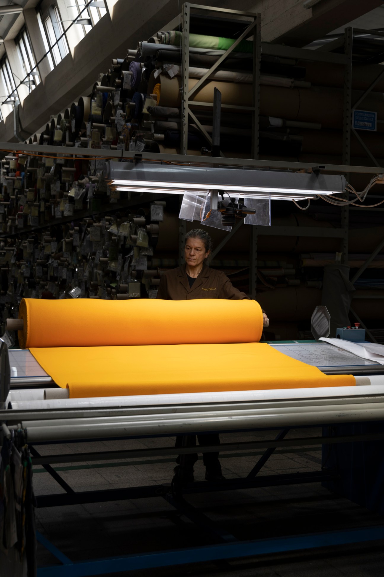 Worker in yellow shirt carefully inspecting bright yellow fabric material at textile manufacturing facility