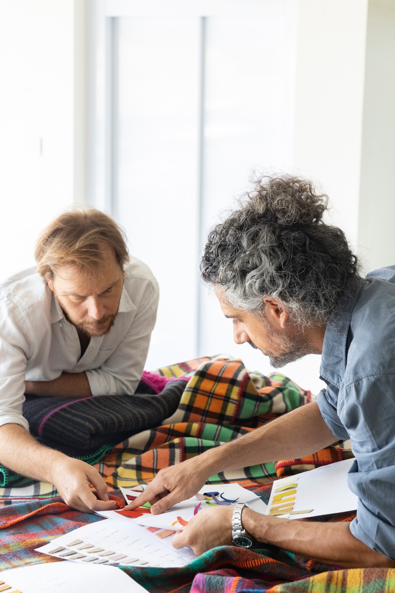 Two men examining fabric samples and color swatches on a colorful plaid blanket