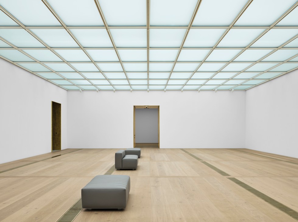 Gallery interior with glass ceiling grid, white walls, wood floors, and gray seating benches
